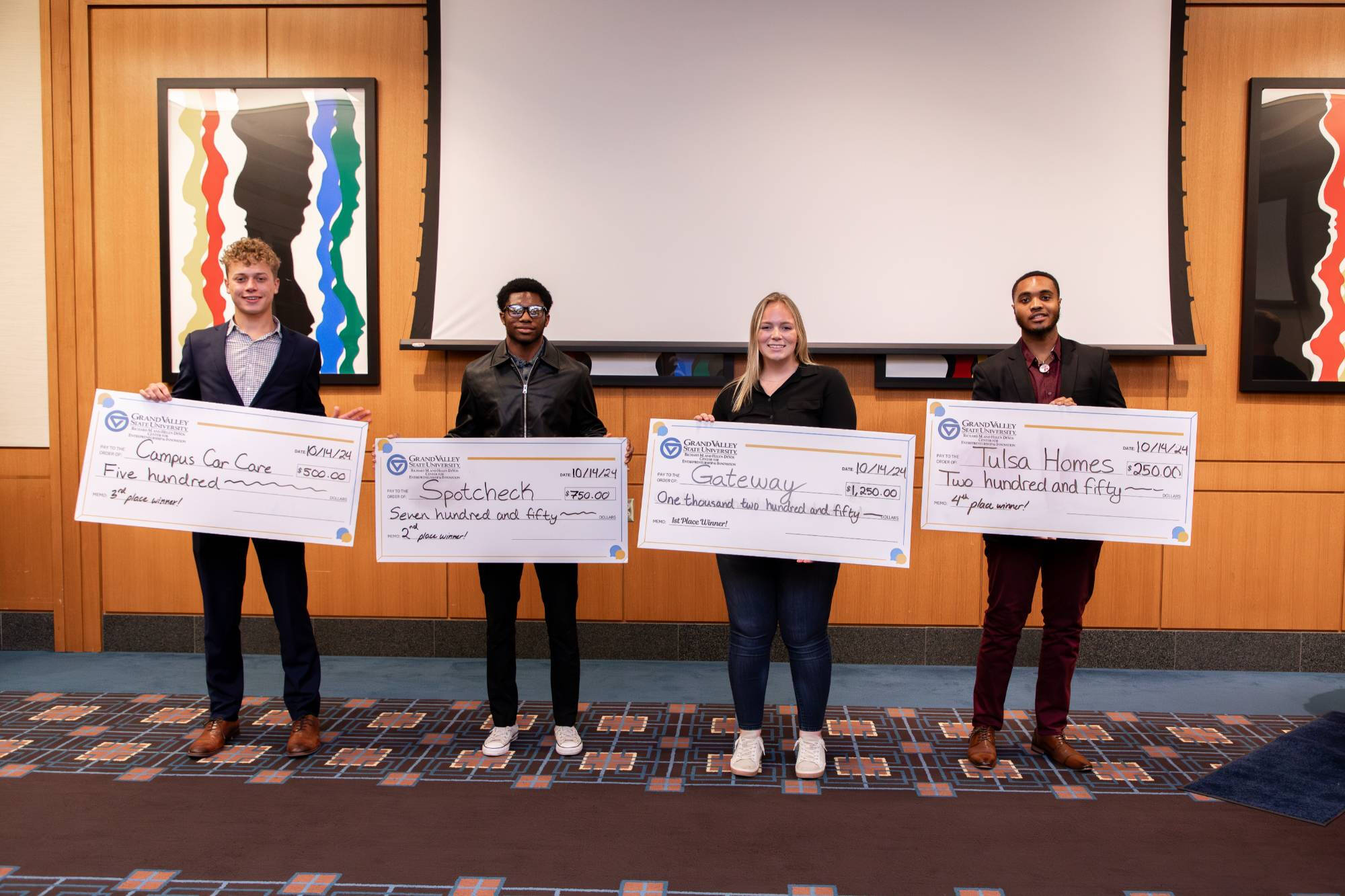 Four students standing in a line for a photo, presenting their award checks at a recent CEO Pitch Competition